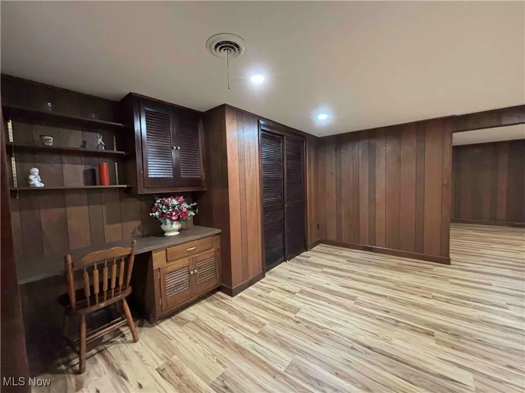 Home office with built in desk, light wood-style flooring, and wood walls