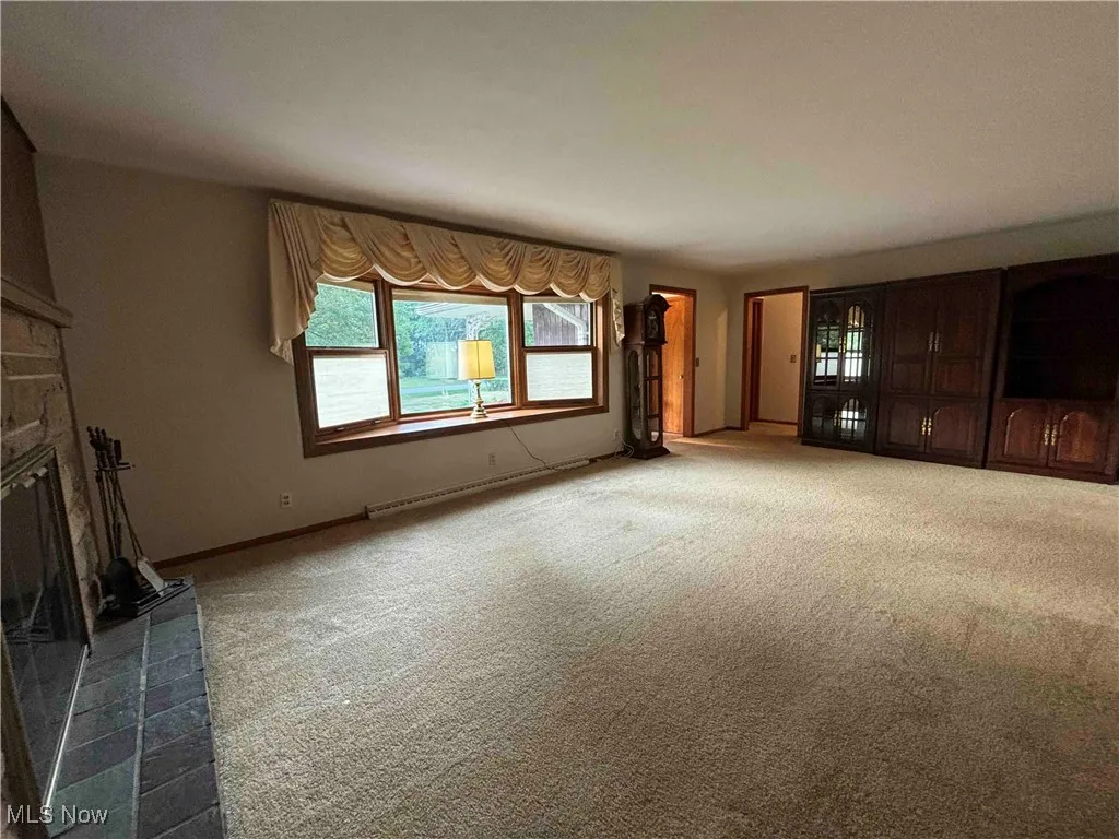 Unfurnished living room with a stone fireplace, carpet, and a baseboard heating unit