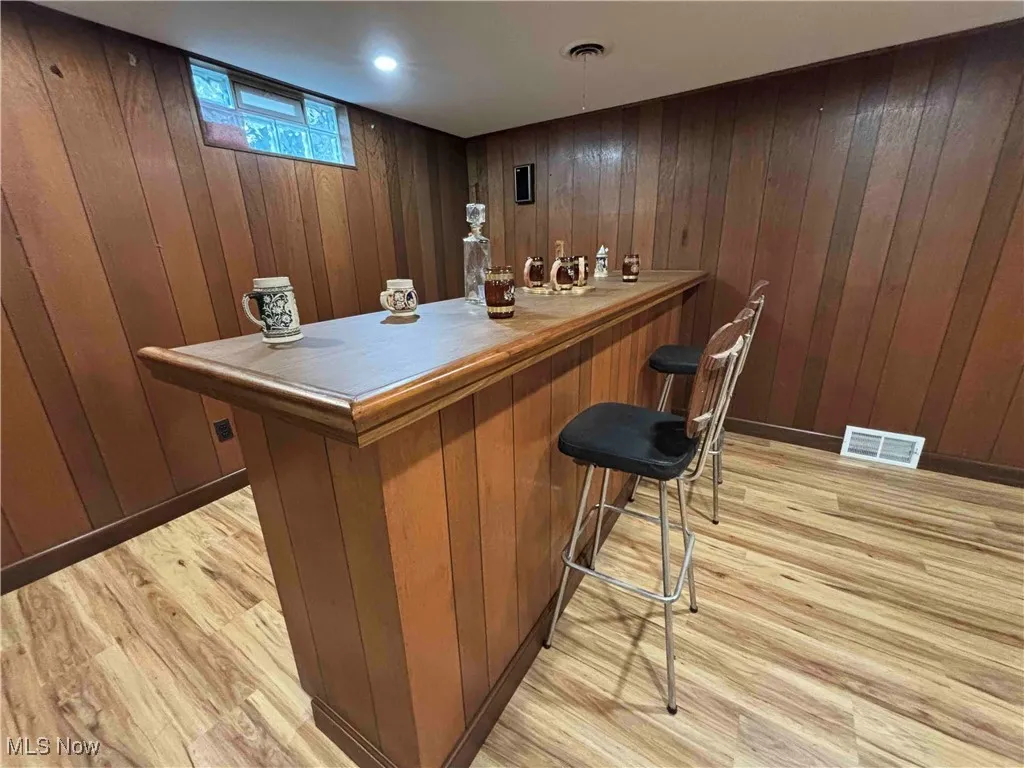 Indoor dry bar featuring light wood-style flooring and wooden walls