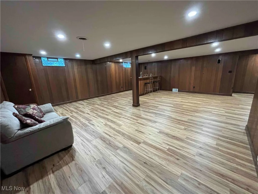 Below grade area featuring light wood-type flooring, recessed lighting, bar area, and wood walls