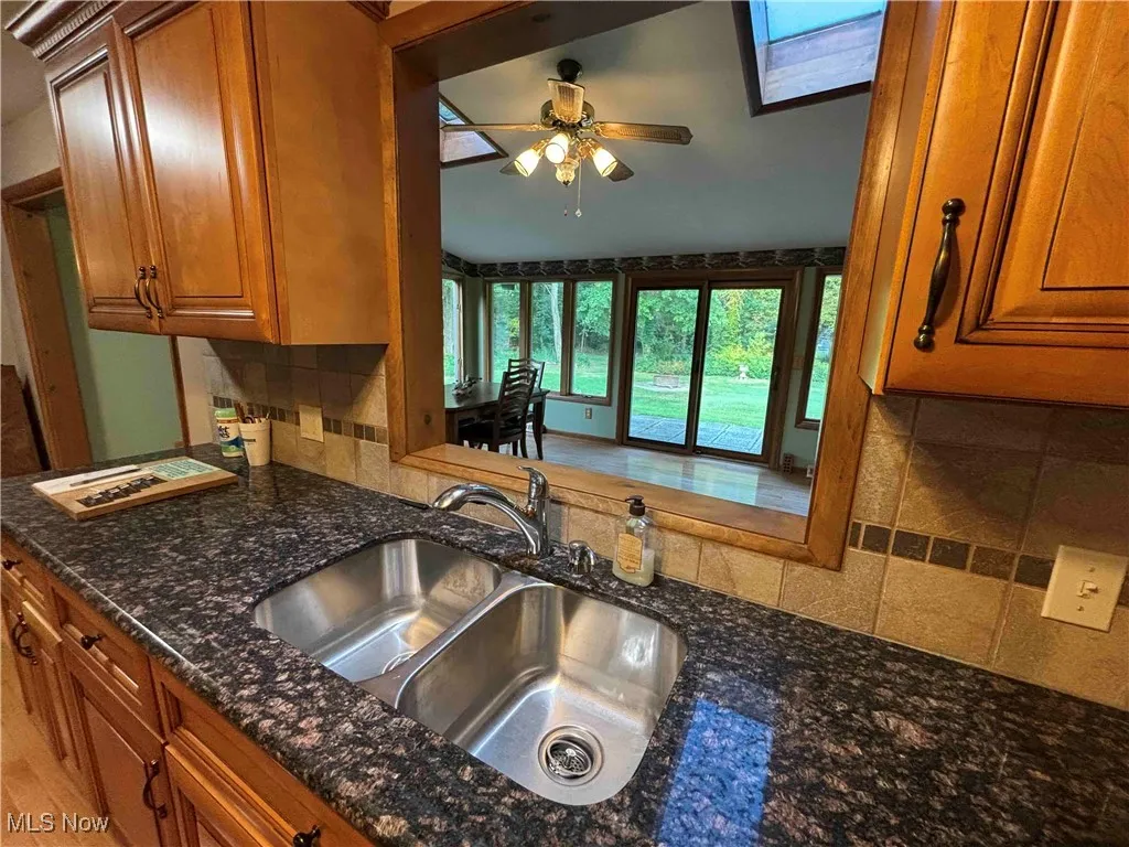 Kitchen with decorative backsplash, brown cabinetry, dark stone countertops, and ceiling fan