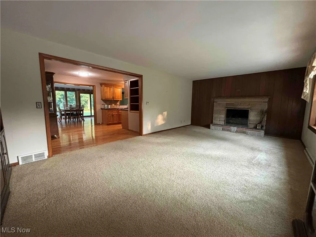 Unfurnished living room with wood walls, light colored carpet, and a stone fireplace