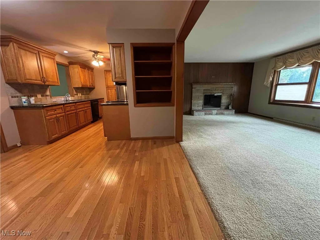 Kitchen featuring brown cabinets, dark countertops, a fireplace, light wood-style floors, and a ceiling fan