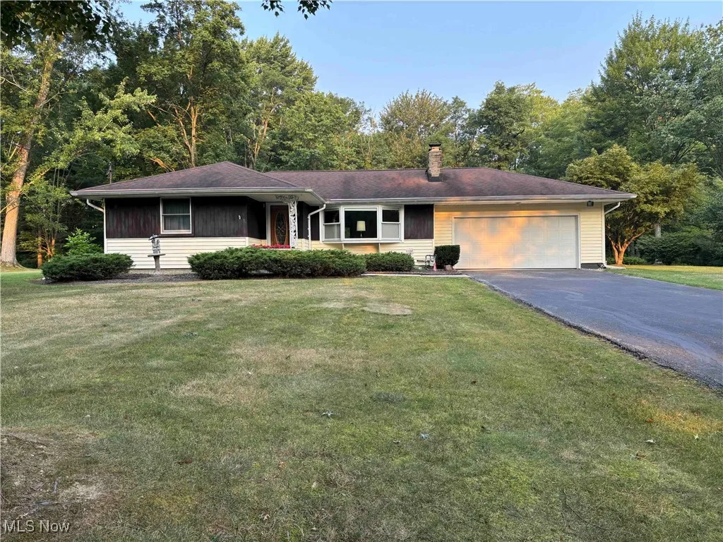 Ranch-style home with driveway, an attached garage, a chimney, and a front yard
