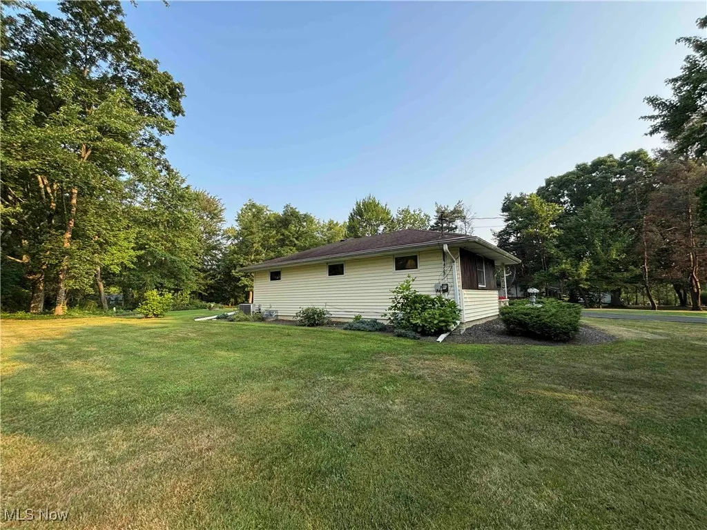 View of home's exterior featuring a lawn and view of wooded area