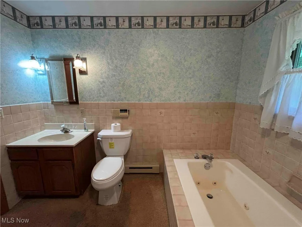 Bathroom featuring wallpapered walls, a wainscoted wall, a whirlpool tub, vanity, and baseboard heating