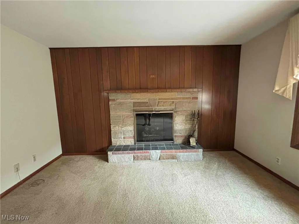 Unfurnished living room with wooden walls, carpet flooring, and a stone fireplace