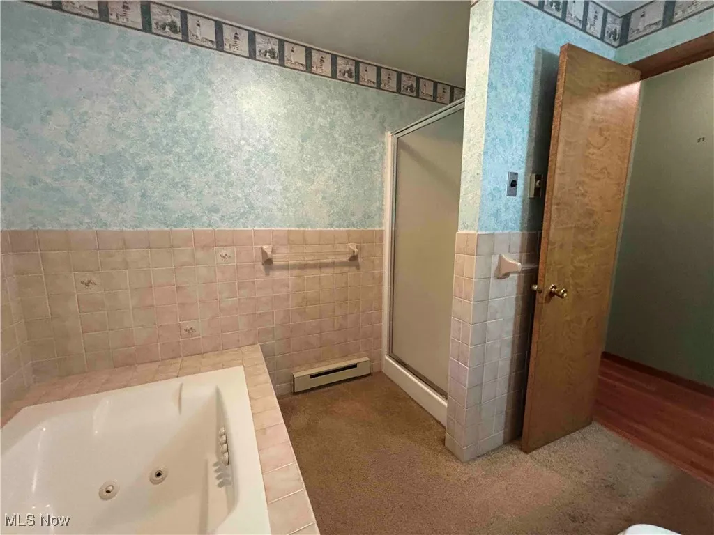 Bathroom with wallpapered walls, a stall shower, a jetted tub, a baseboard heating unit, and wainscoting