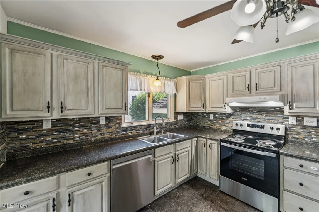 Kitchen with appliances with stainless steel finishes, ornamental molding, backsplash, dark countertops, and under cabinet range hood