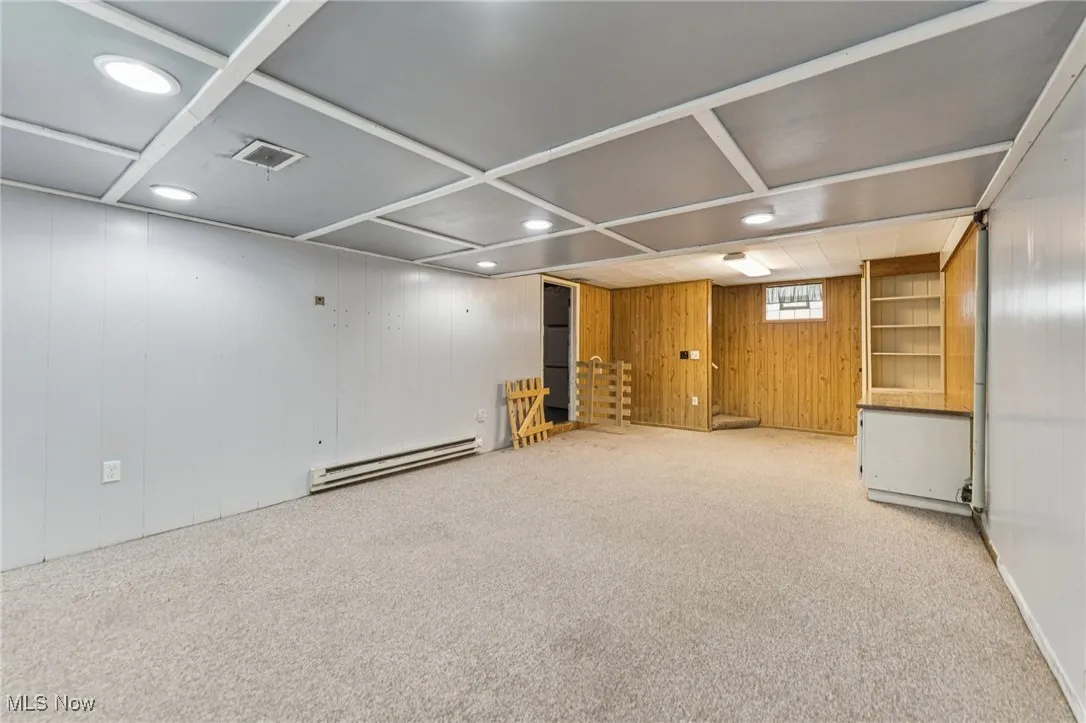 Carpeted spare room featuring wooden walls, a baseboard heating unit, and recessed lighting