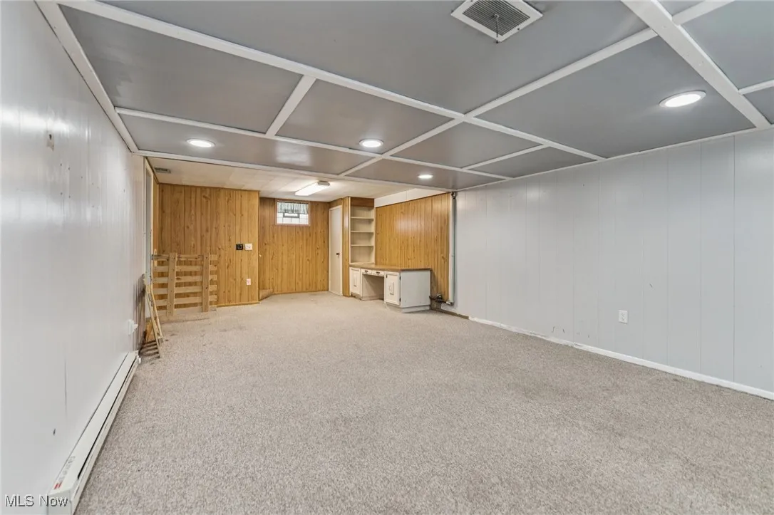Below grade area featuring a baseboard radiator, wood walls, recessed lighting, and light colored carpet