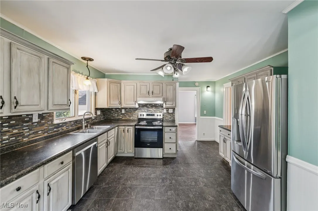 Kitchen with a wainscoted wall, appliances with stainless steel finishes, dark countertops, crown molding, and decorative backsplash