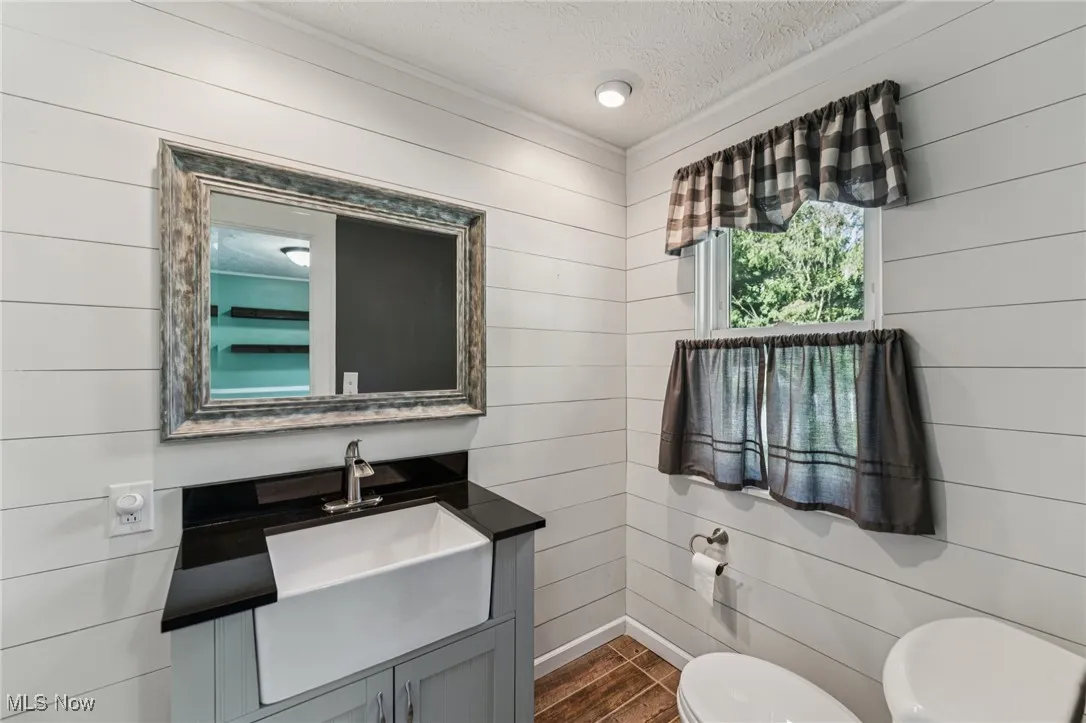 Half bath with a textured ceiling, vanity, and wood walls