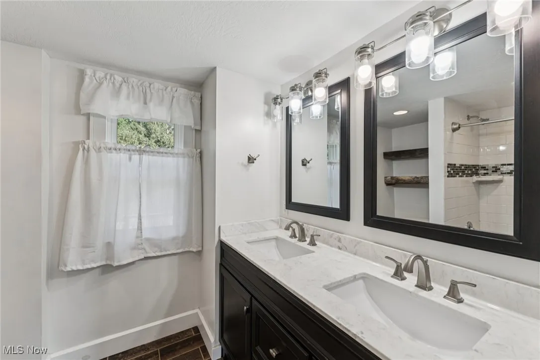 Full bath featuring double vanity, a shower, a textured ceiling, and wood finished floors