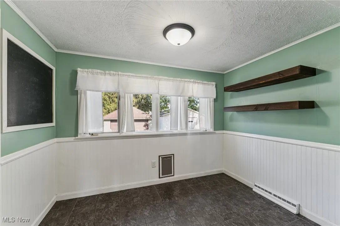 Spare room with wainscoting, a textured ceiling, a baseboard radiator, and ornamental molding