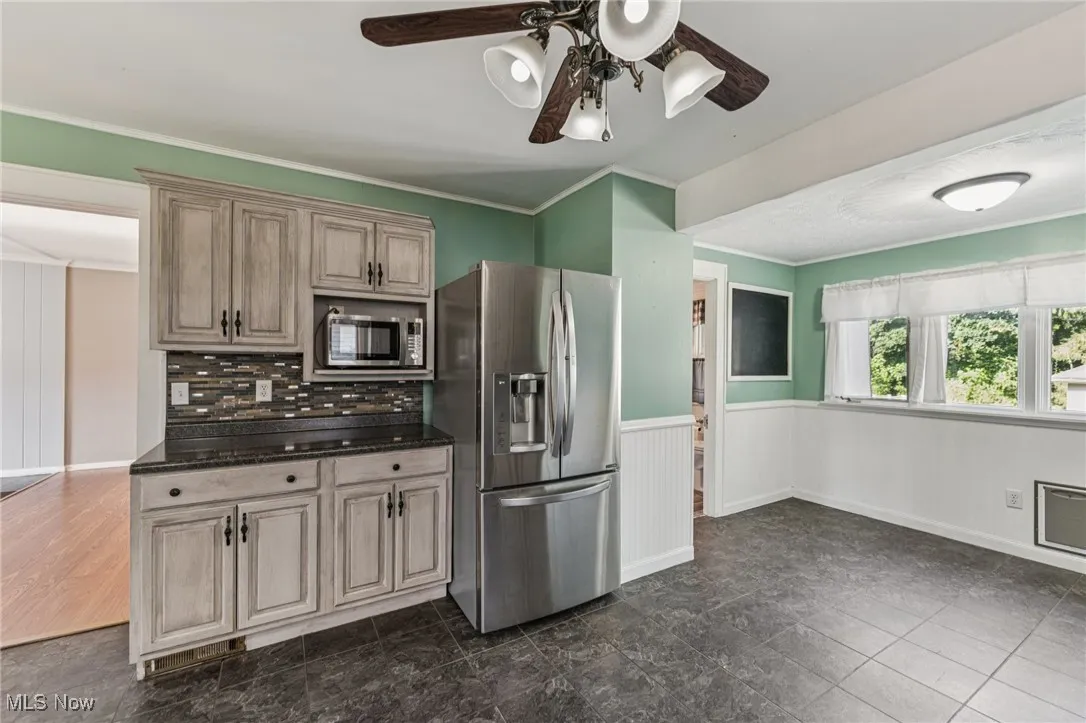 Kitchen featuring stainless steel appliances, a wainscoted wall, crown molding, ceiling fan, and dark stone counters