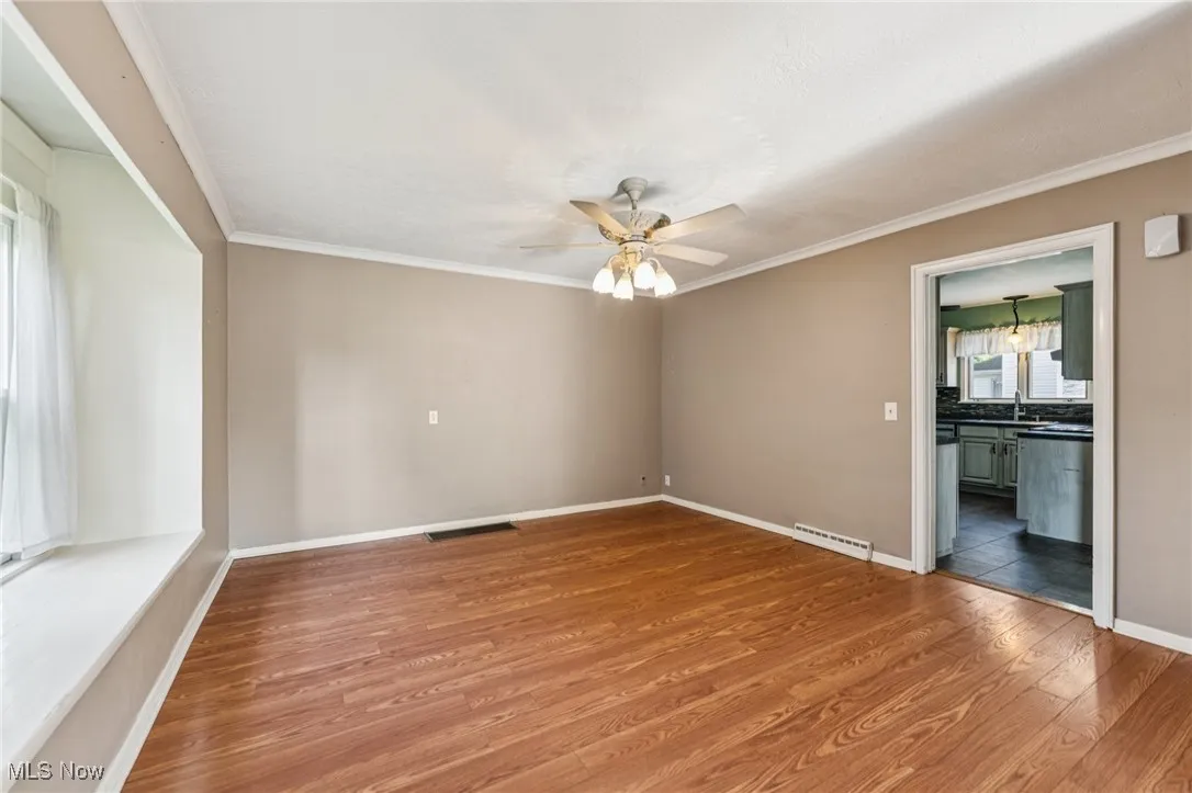 Empty room with crown molding, wood finished floors, and a ceiling fan