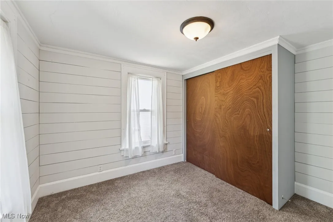 Unfurnished bedroom featuring wood walls, carpet, a closet, and ornamental molding