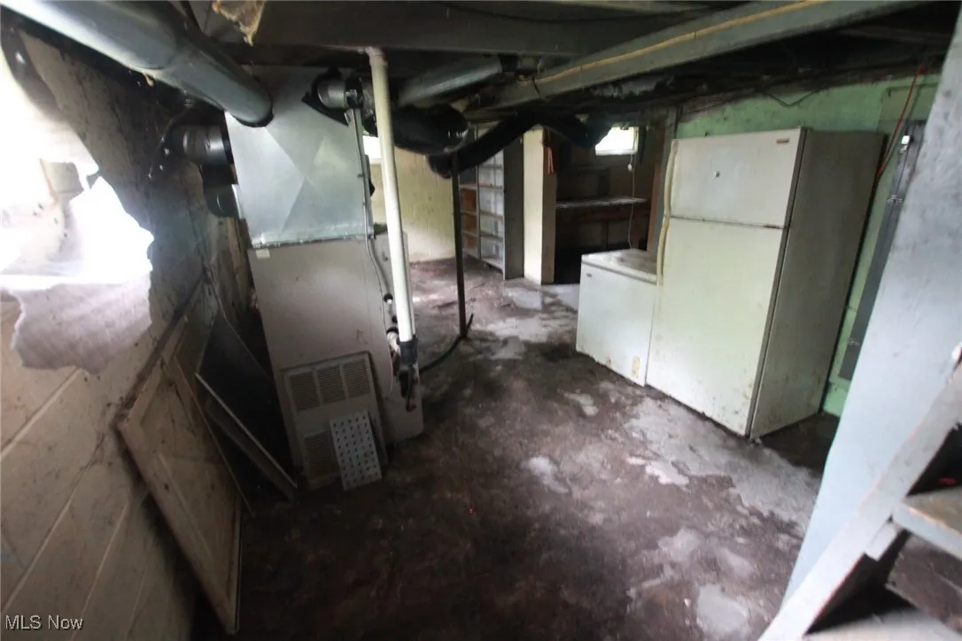 Unfinished basement with freestanding refrigerator and heating unit