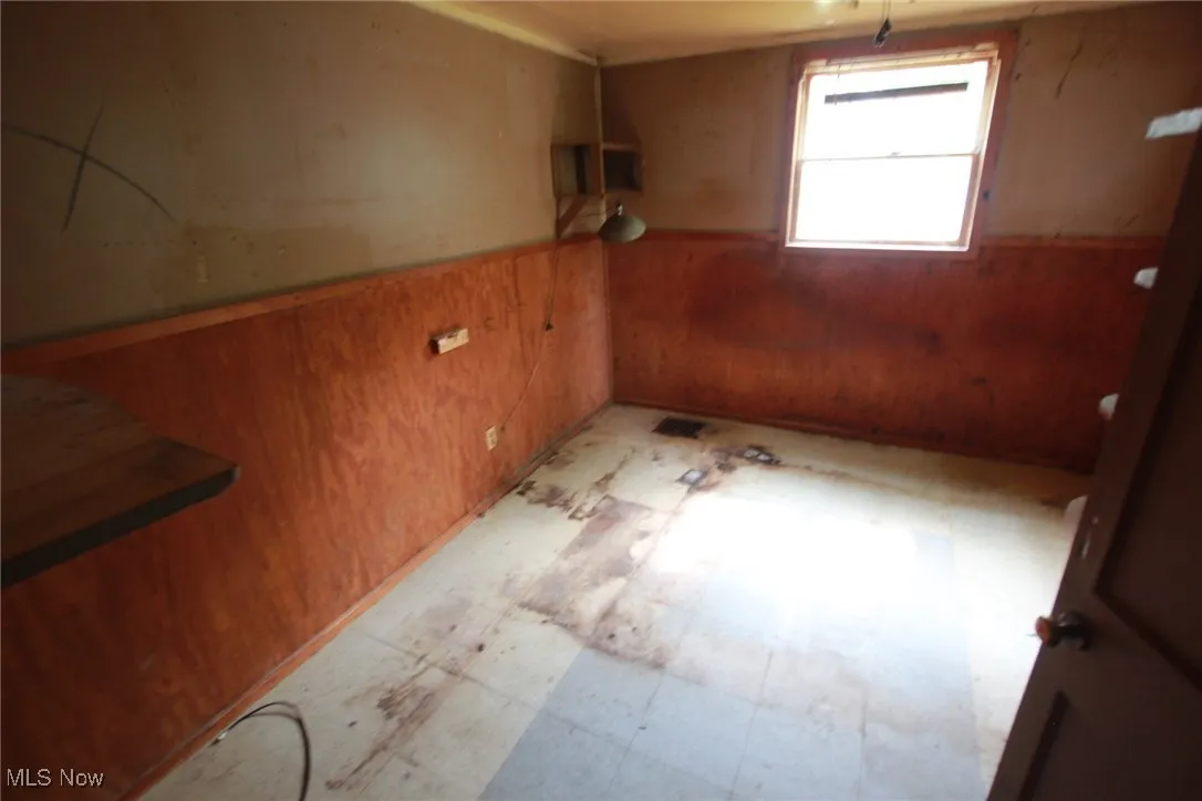 Spare room featuring wood walls, light floors, and wainscoting