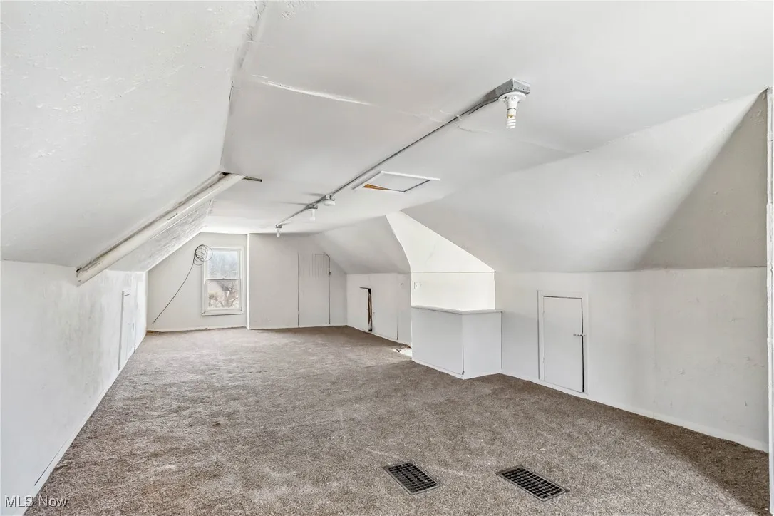 Additional living space featuring lofted ceiling, visible vents, and light colored carpet
