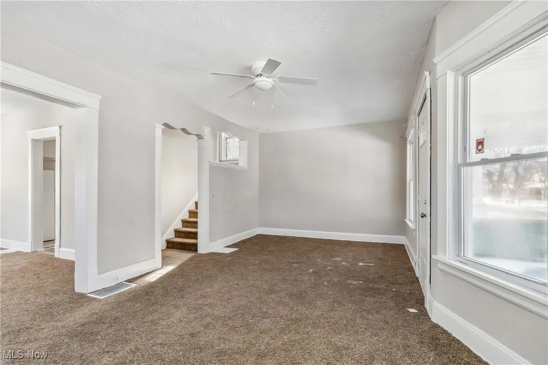 Empty room featuring a ceiling fan, baseboards, dark carpet, and a textured ceiling