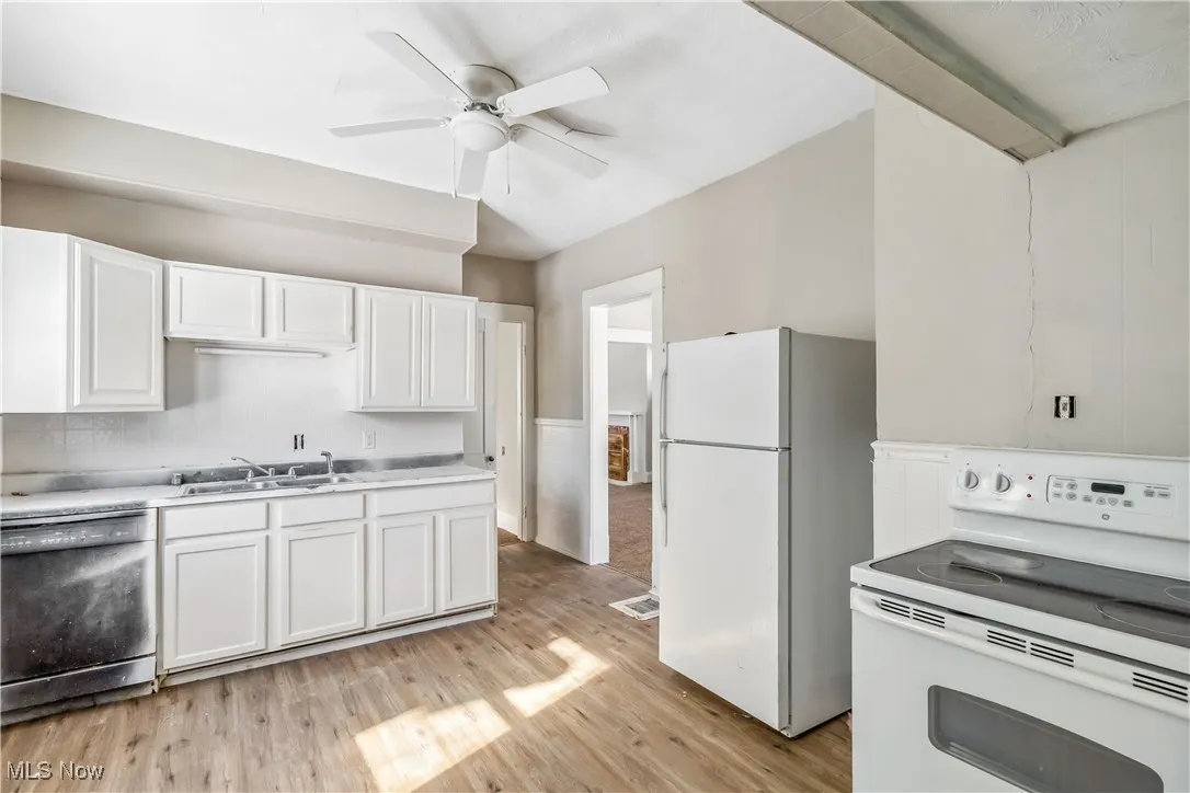 Kitchen featuring light wood-style flooring, white appliances, a sink, white cabinets, and light countertops