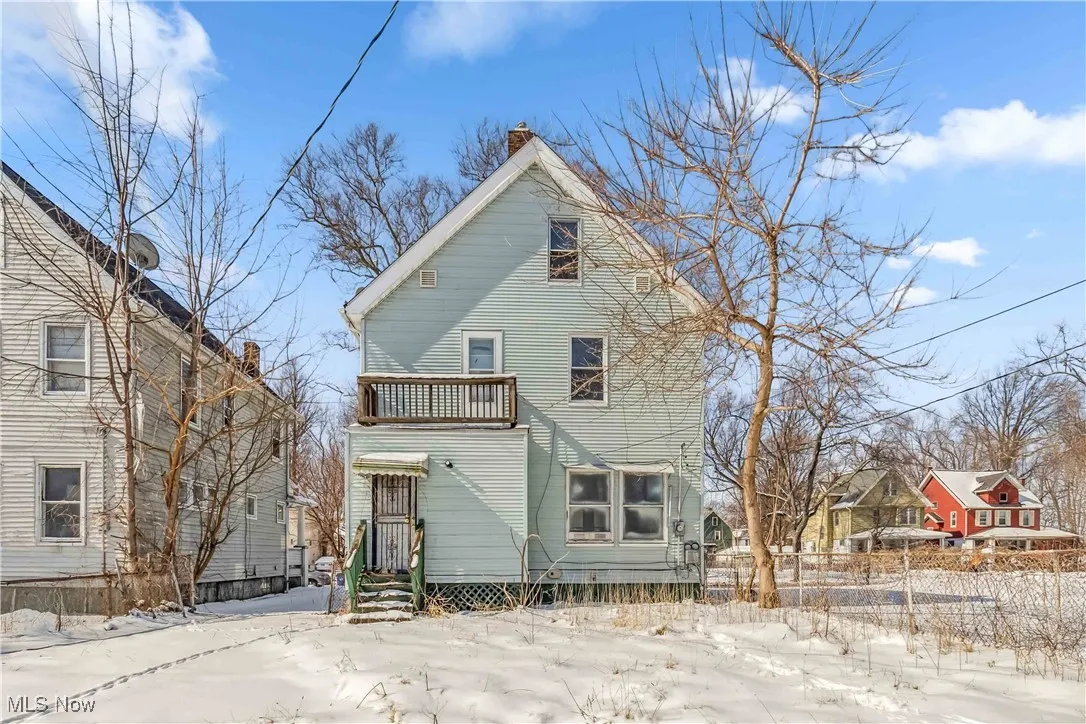 Snow covered house featuring a chimney, fence, and a balcony