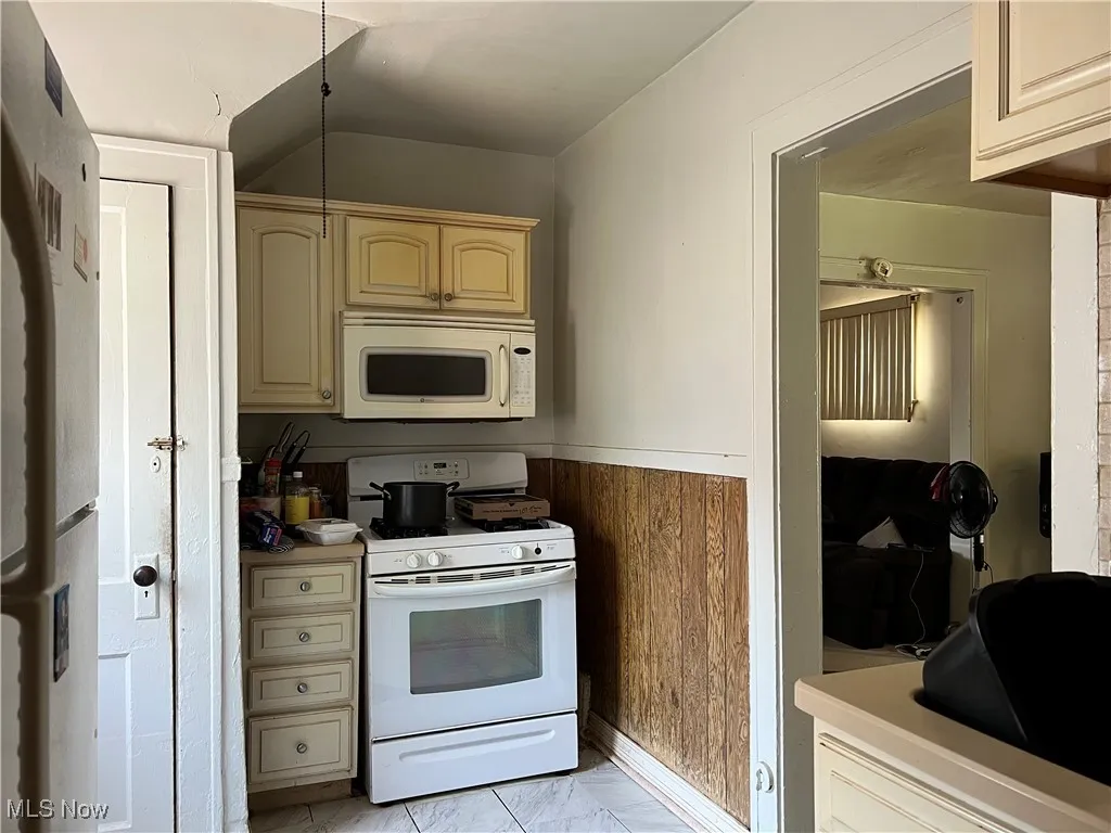 Kitchen featuring white appliances, light countertops, cream cabinetry, wood walls, and wainscoting