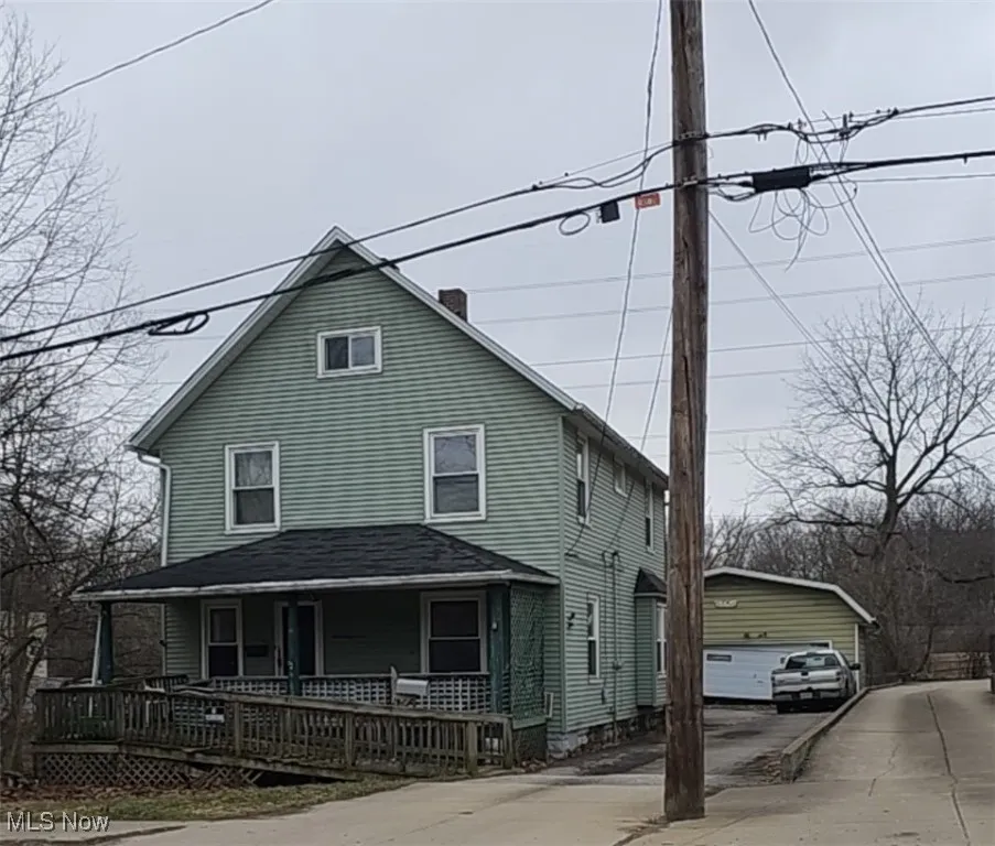 View of front of home featuring covered porch, an outdoor structure, a chimney, and a garage