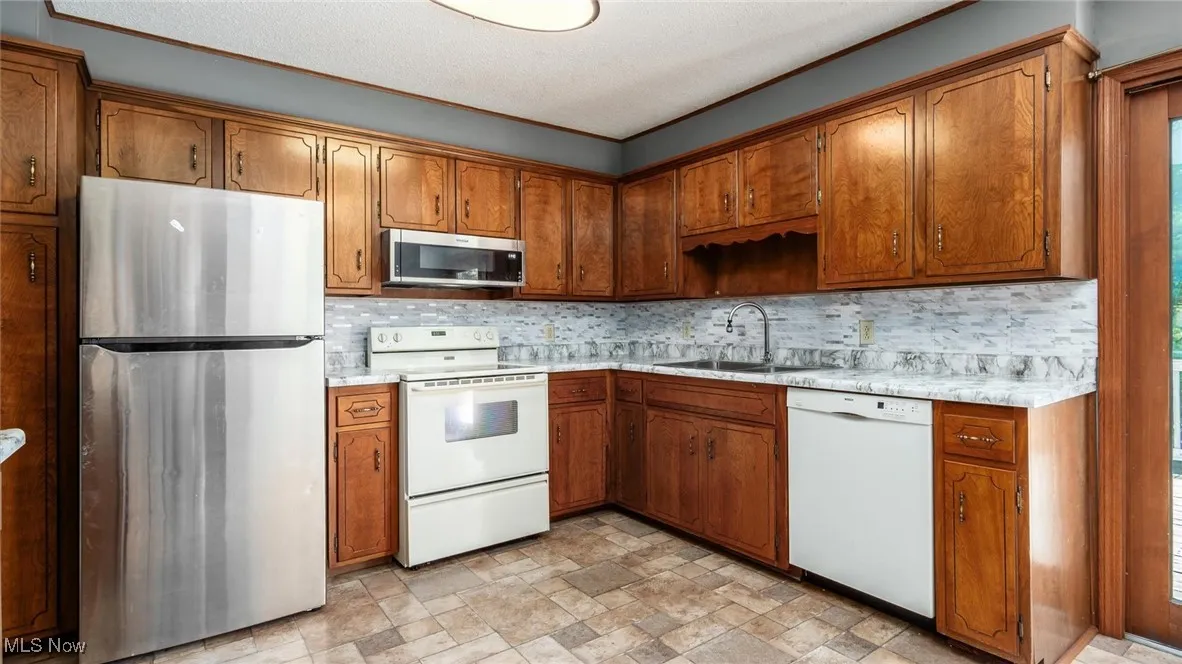 Kitchen featuring appliances with stainless steel finishes, stone finish floors, and brown cabinetry