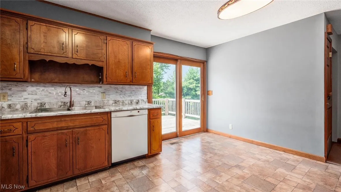 Kitchen with stone finish flooring, white dishwasher, backsplash, light countertops, and a textured ceiling