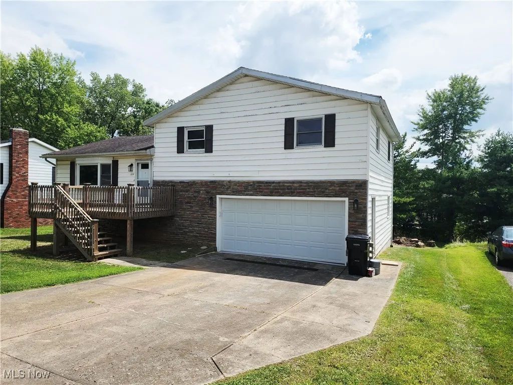 Split level home with a garage, a deck, a front yard, concrete driveway, and stairs