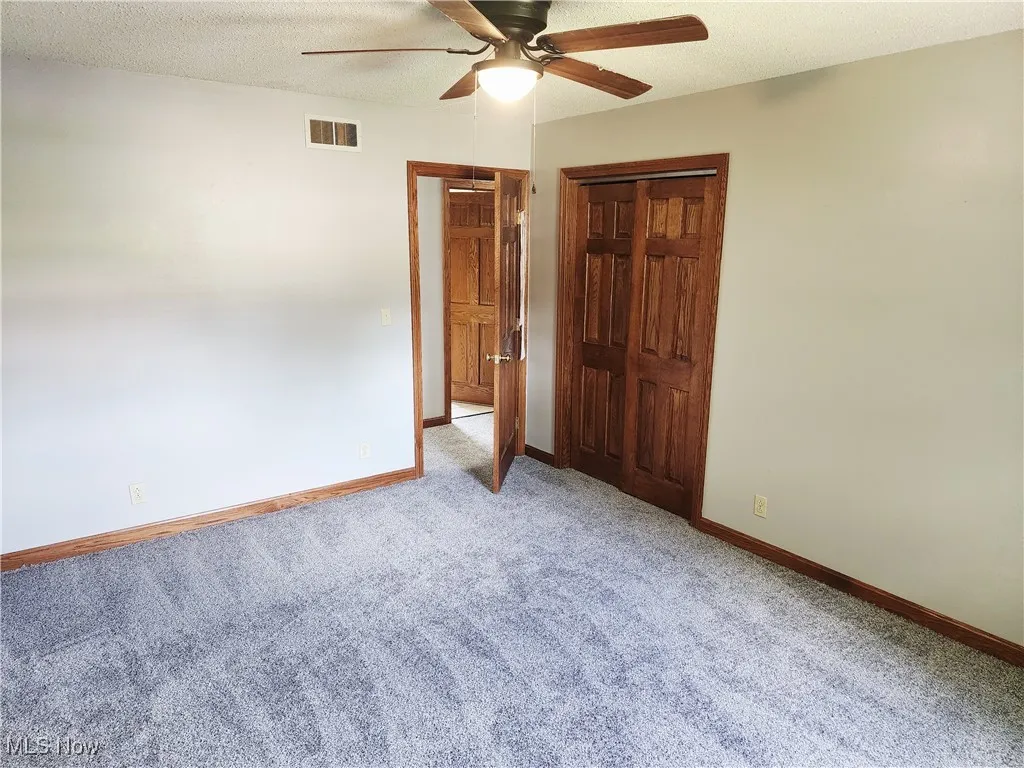 Unfurnished bedroom with a textured ceiling, light colored carpet, a closet, and ceiling fan