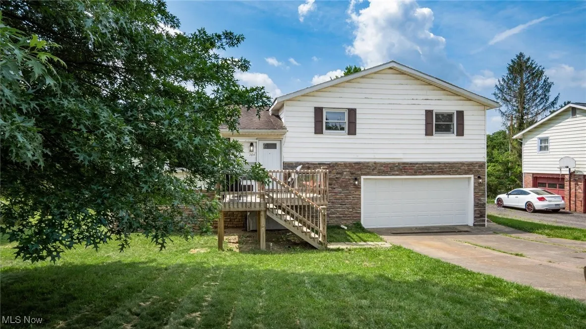 View of front of house with a garage, concrete driveway, a front lawn, stairs, and stone siding