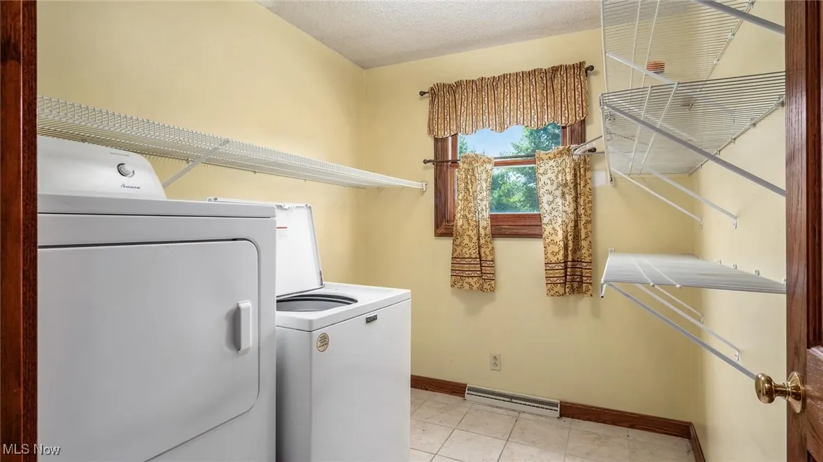 Washroom with independent washer and dryer, a textured ceiling, and light tile patterned floors