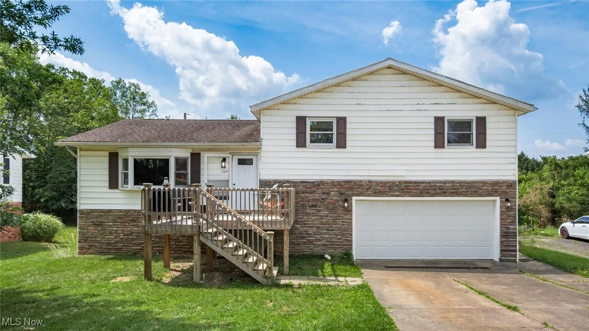 Split level home featuring a garage, a front yard, driveway, stone siding, and a deck