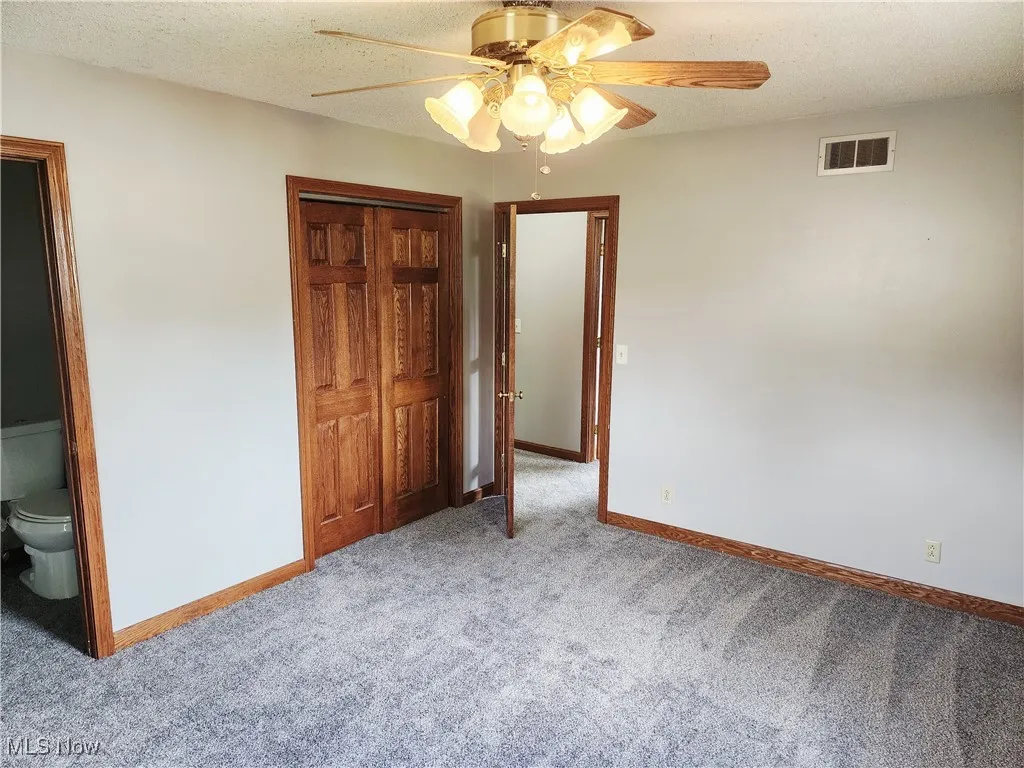 Unfurnished bedroom featuring a textured ceiling, carpet, a closet, a ceiling fan, and connected bathroom