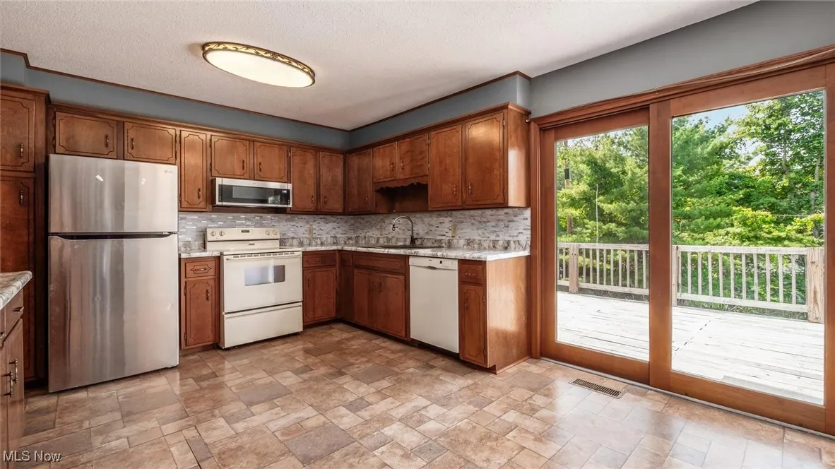 Kitchen with stainless steel appliances, stone finish floors, light countertops, decorative backsplash, and brown cabinetry