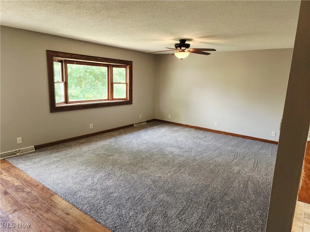 Unfurnished room with a textured ceiling, carpet flooring, wood finished floors, and a ceiling fan