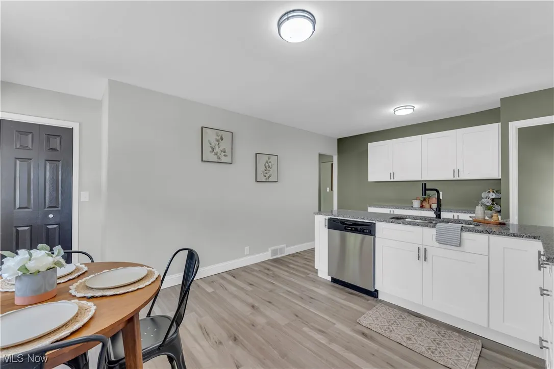 Kitchen featuring light wood-style floors, dark stone counters, dishwasher, and white cabinets