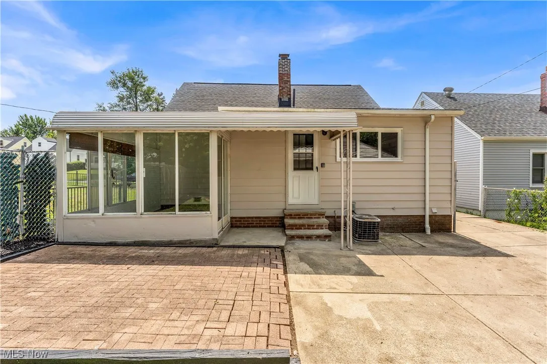 Rear view of property with a sunroom, a chimney, a patio, entry steps, and a shingled roof