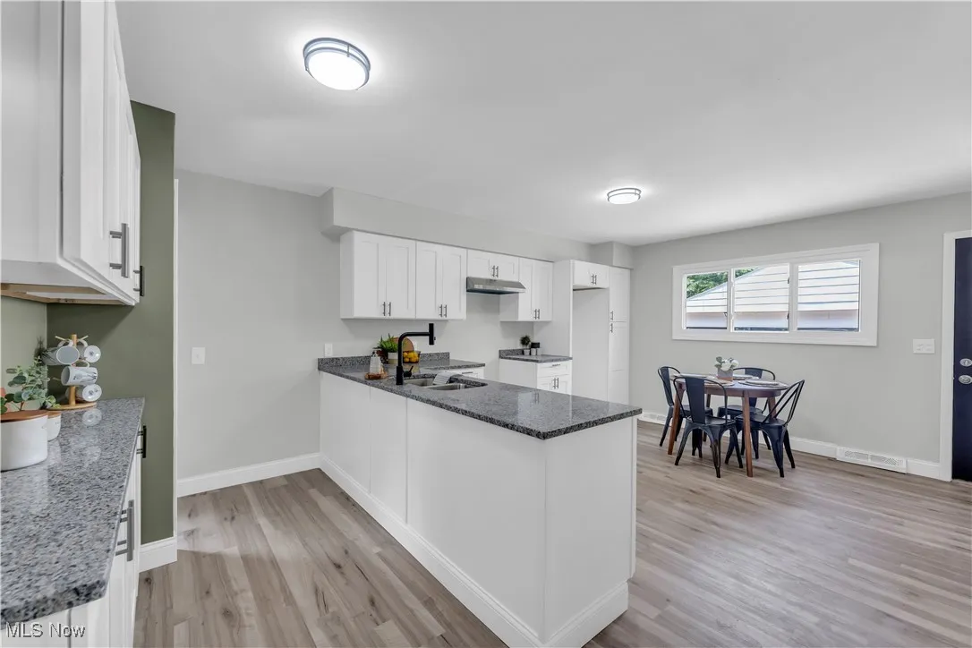 Kitchen featuring a peninsula, dark stone counters, white cabinets, light wood finished floors, and under cabinet range hood