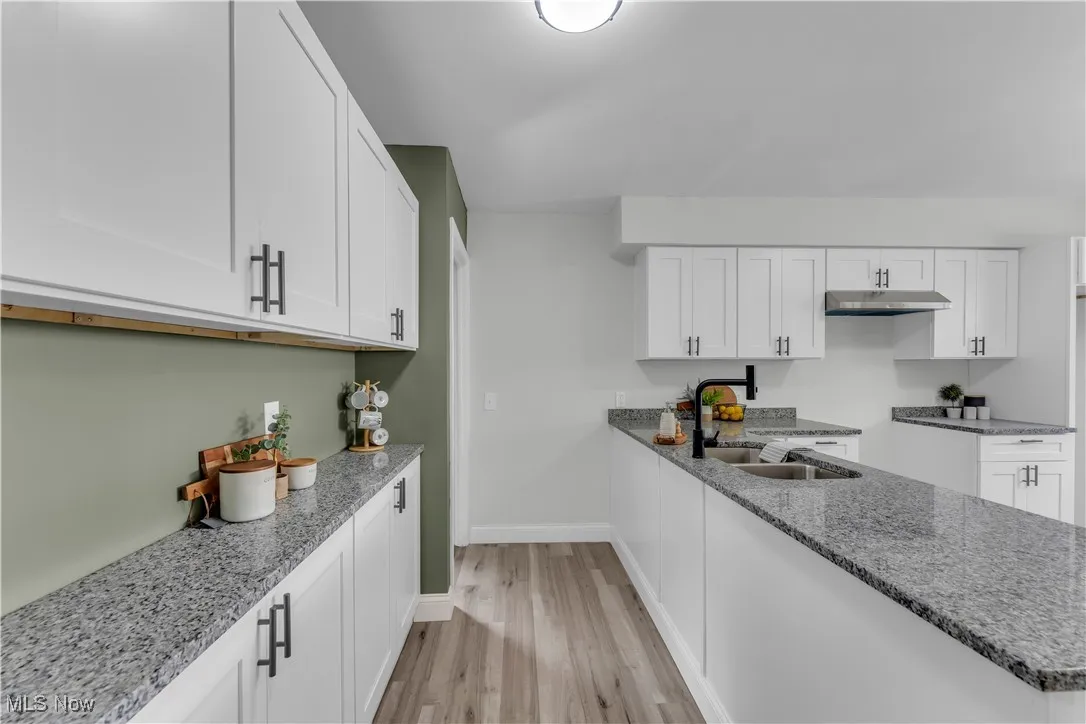 Kitchen with light stone counters, light wood-style flooring, and white cabinetry