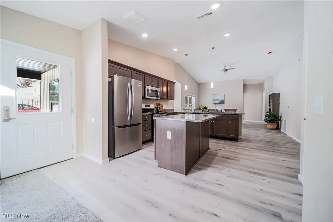 Kitchen with stainless steel appliances, a kitchen island, healthy amount of natural light, lofted ceiling, and dark brown cabinetry