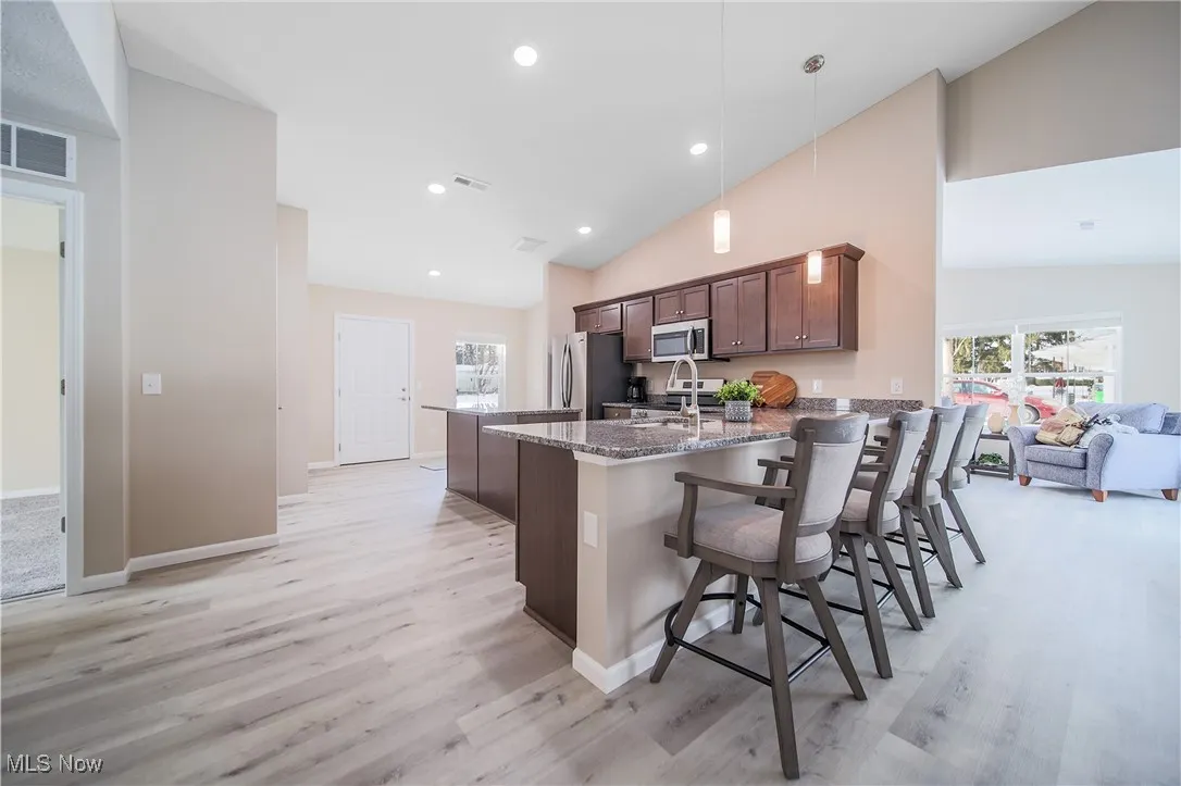 Kitchen with vaulted ceiling, a peninsula, light stone countertops, appliances with stainless steel finishes, and light wood finished floors