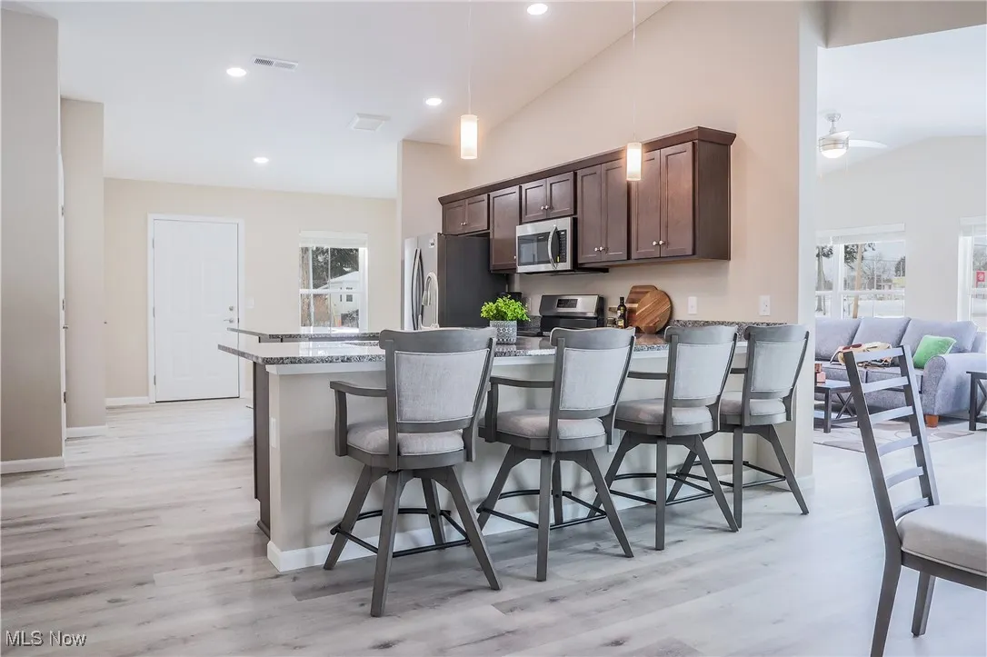 Kitchen with vaulted ceiling, a breakfast bar, stainless steel appliances, light wood finished floors, and dark brown cabinetry