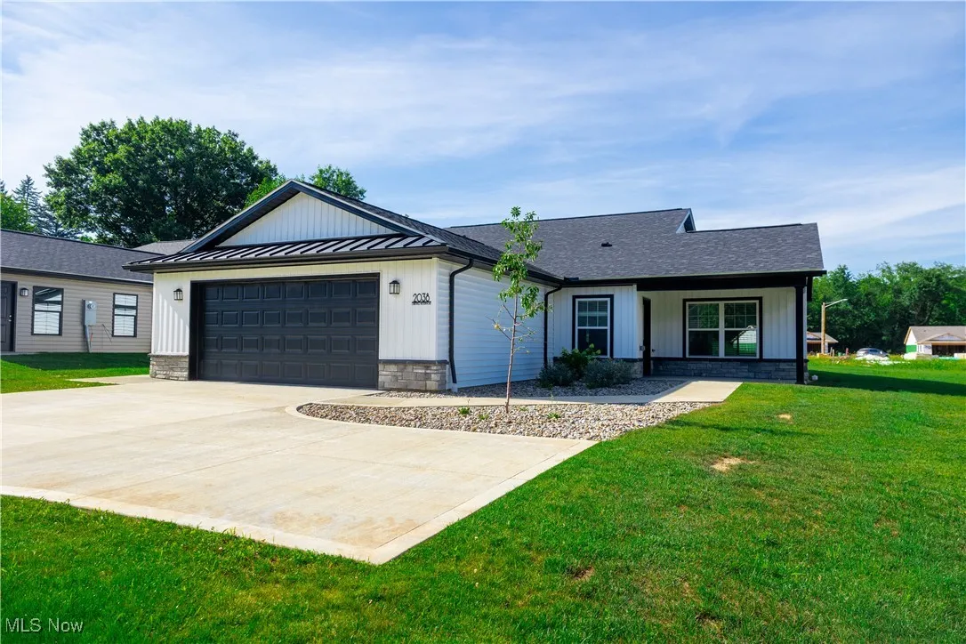 View of front facade featuring a front lawn, stone siding, an attached garage, driveway, and board and batten siding