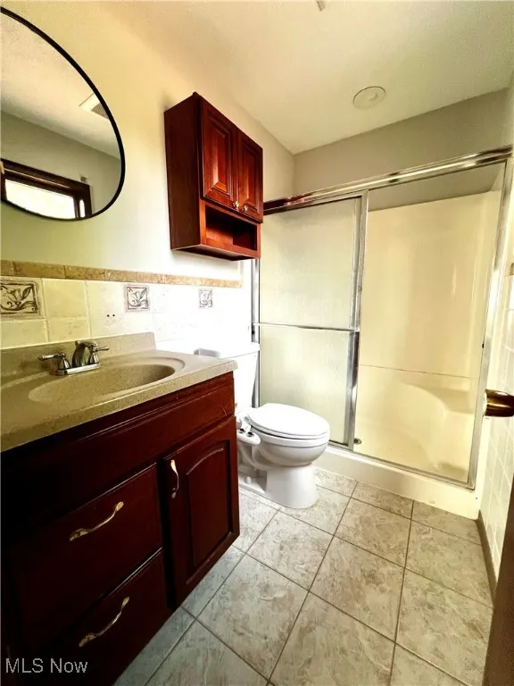 Primary bathroom with vanity, a shower stall, tile walls, and tile patterned floors