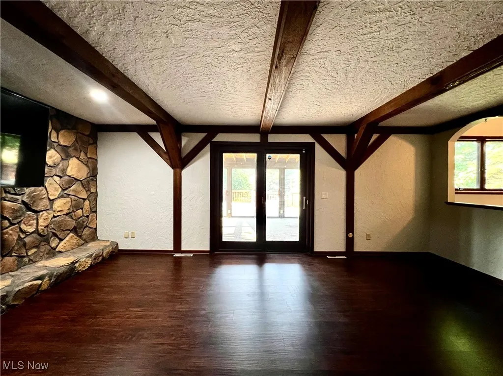 Unfurnished living room featuring a textured wall, healthy amount of natural light, a textured ceiling, wood finished floors, and beamed ceiling